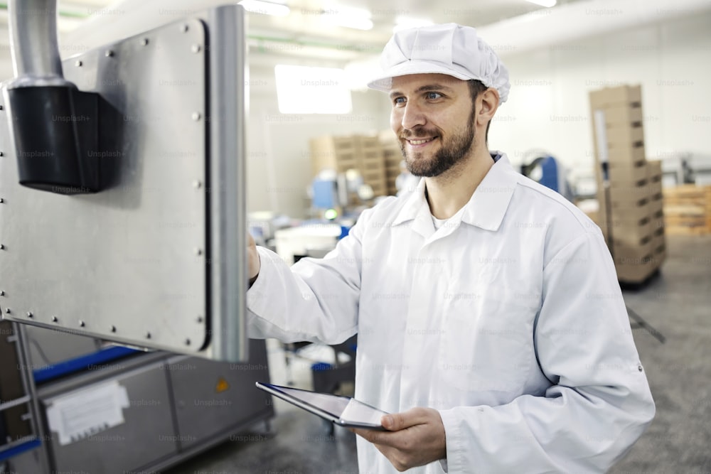 A meat industry worker holds a tablet in his hands and programs a meat packing machine.