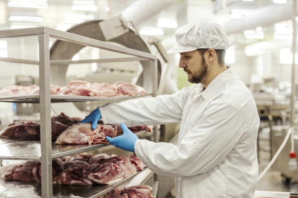 A meat industry worker is taking fresh piece of meat and preparing it for further processing.
