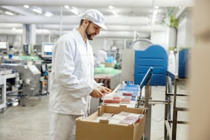 A meat industry laborer is packing minced meat into a box and getting ready to deliver it while standing next to a conveyor belt.