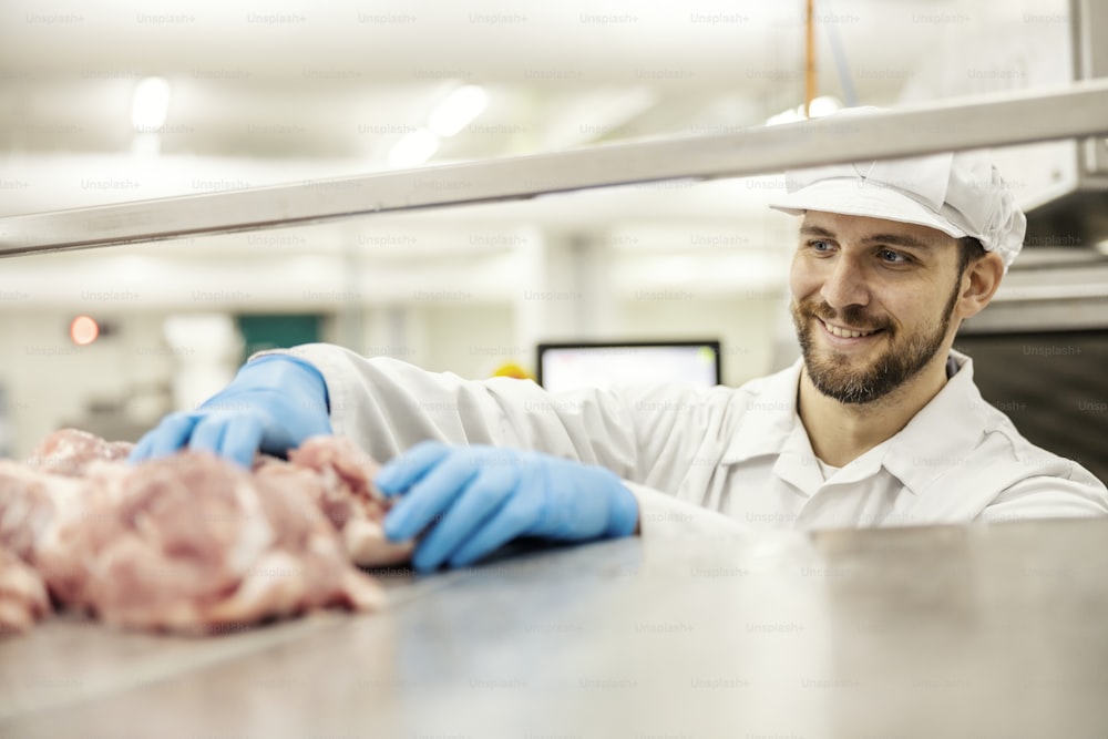 A meat factory worker is putting raw meat into a grinding machine.