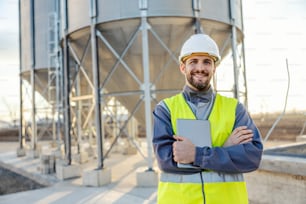 A manager is standing in front of the silos full of supplies and smiling at the camera.