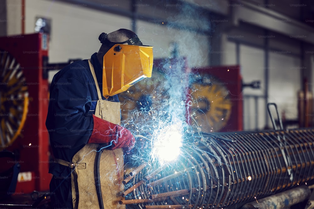 Um metalúrgico da indústria pesada está soldando uma estrutura de metal com uma máquina de solda em uma fábrica.