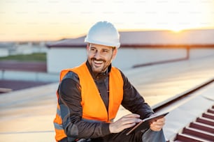 A smiling worker scrolling on tablet on the roof.