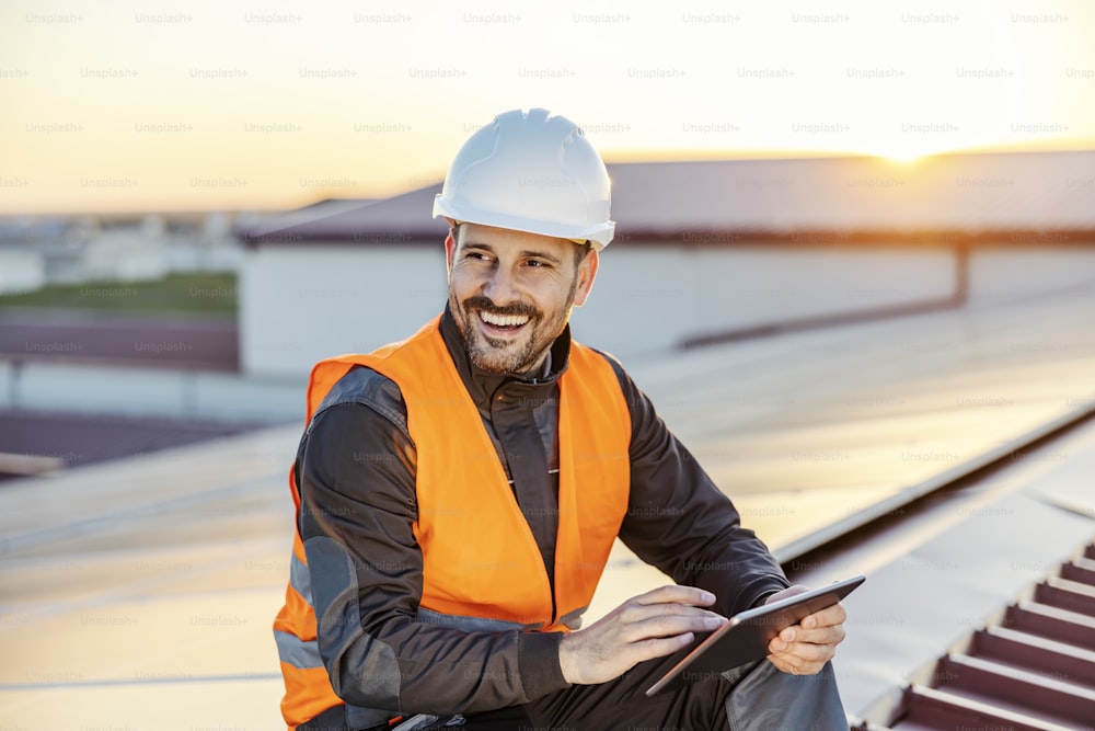 Um trabalhador sorridente rolando no tablet no telhado.