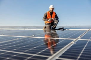 Um trabalhador sorrindo para a câmera e segurando chave de fenda para instalar painéis solares no telhado.