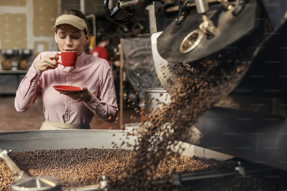 Una supervisora de fábrica bebiendo una taza de café aromático junto a una tostadora.