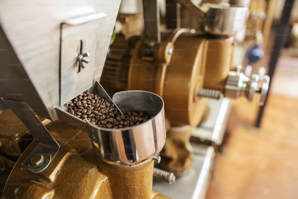 Close up of coffee grinding machine with coffee beans in factory.