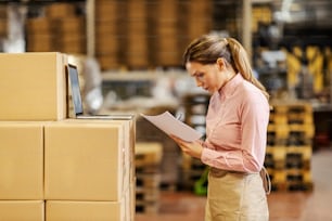 A female food factory worker standing in warehouse and checking on goods.