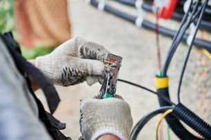 Man electrician installing solar panel system. Close up technician hands in gloves making electrical wiring inverter and electric box. Concept of alternative and renewable energy.