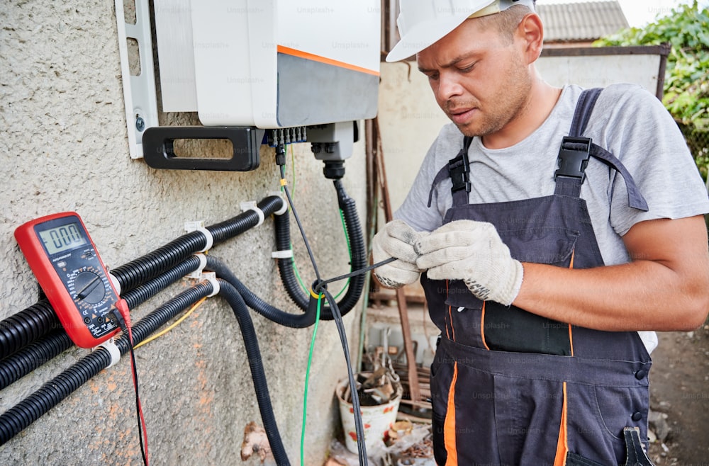 Man electrician installing solar panel system. Inspector in gloves making electrical wiring inverter and electric box. Concept of alternative and renewable energy.