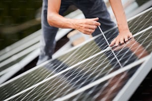 Operaio che monta moduli solari fotovoltaici sul tetto della casa. Primo piano dell'elettricista che installa il sistema di pannelli solari all'aperto, stringendo con chiave esagonale. Concetto di energia alternativa e rinnovabile.