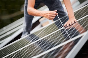 Man worker mounting photovoltaic solar moduls on roof of house. Close up of electrician installing solar panel system outdoors, tightening with hex key. Concept of alternative and renewable energy.