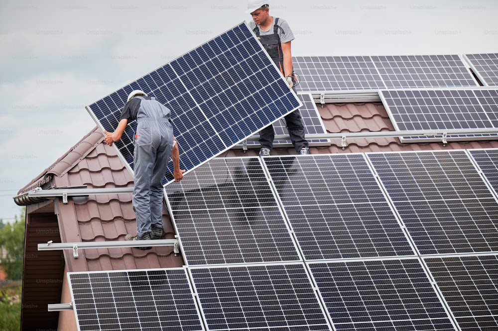 Operai che montano moduli solari fotovoltaici sul tetto della casa. Elettricisti in caschi che installano sistemi di pannelli solari all'aperto. Concetto di energia alternativa e rinnovabile.