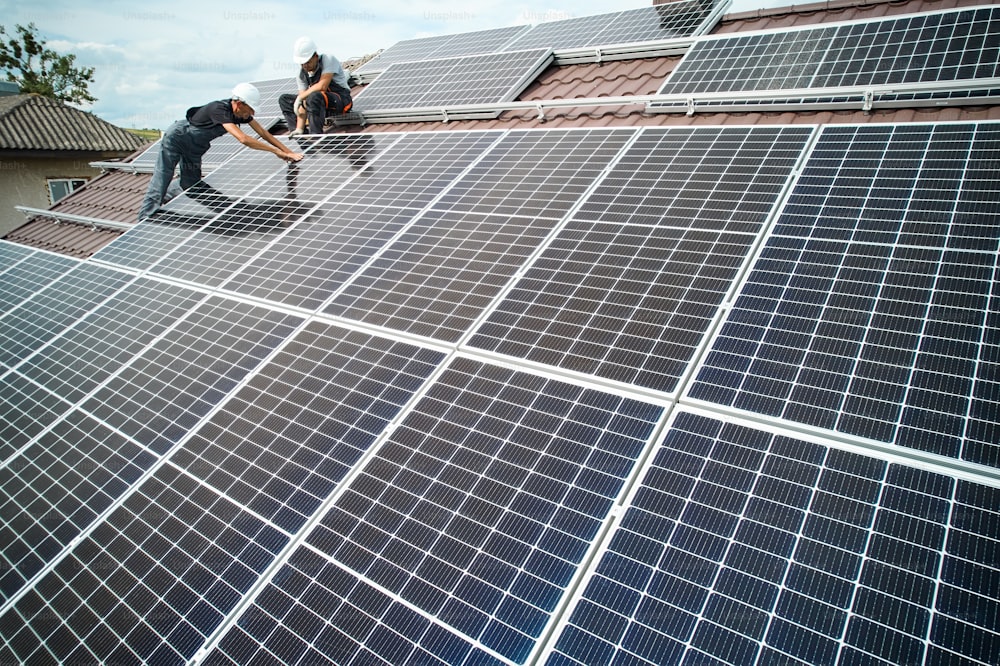 Man technician mounting photovoltaic solar moduls on roof of house. Mounter in helmet installing solar panel system outdoors. Concept of alternative and renewable energy. Aerial view.