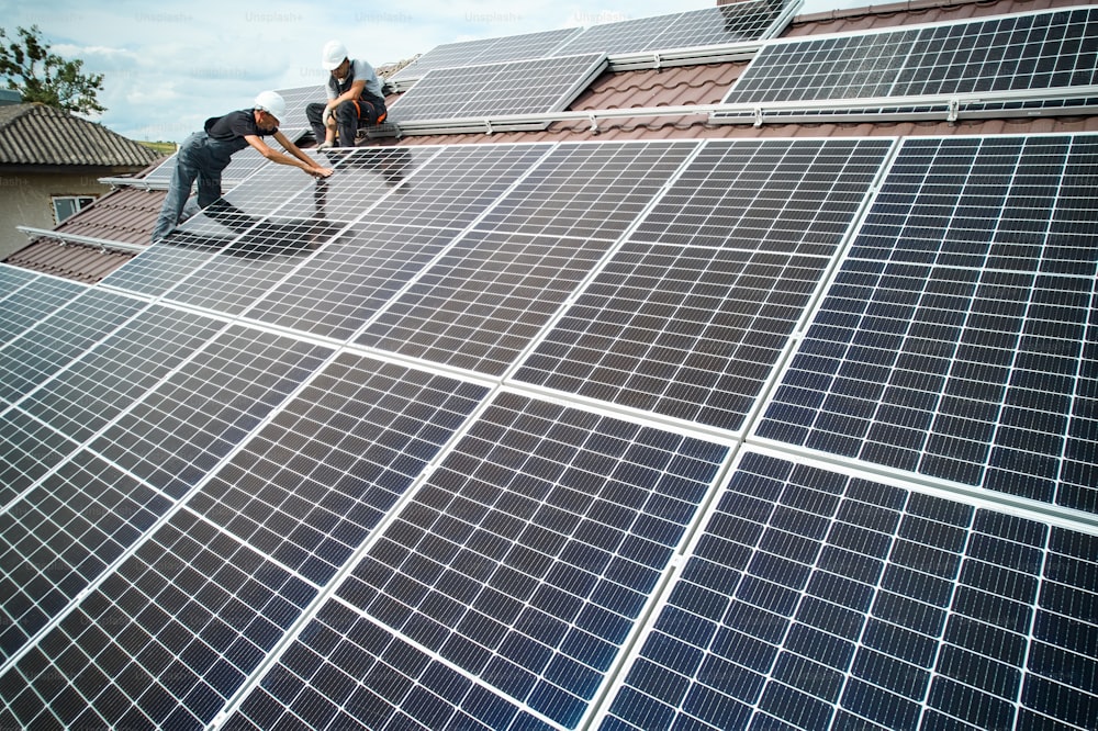 家の屋根に太陽光発電モジュールを取り付ける男性技術者。ソーラーパネルシステムを屋外に設置するヘルメットのマウンター。代替エネルギーと再生可能エネルギーのコンセプト。航空写真。