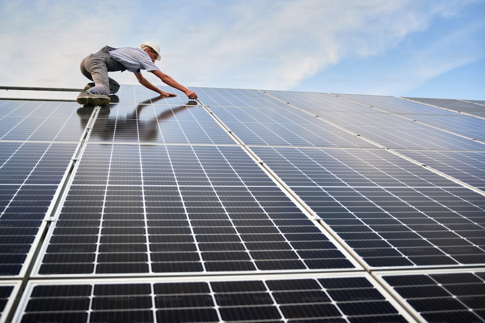 Trabajador masculino montando el sistema de paneles solares fotovoltaicos al aire libre. Ingeniero de hombre colocando módulo solar sobre rieles metálicos. Energía renovable y ecológica.