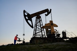 Capable professional inspector checking serviceability of pump jack during shift job at crude oil station, Caucasian man developing drilling rig and extract natural resources at refinery digger