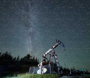 Schöne Aussicht auf den Petroleumpumpenheber unter dem Nachthimmel mit Sternen. Herrliche Landschaft des nächtlichen Ölfeldes mit Ölpumpen-Wippmaschine. Konzept der Erdölindustrie und Ölförderung.