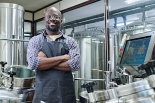 Ritratto di ingegnere afroamericano sorridente alla macchina fotografica in piedi con le braccia incrociate, che lavora nel birrificio moderno