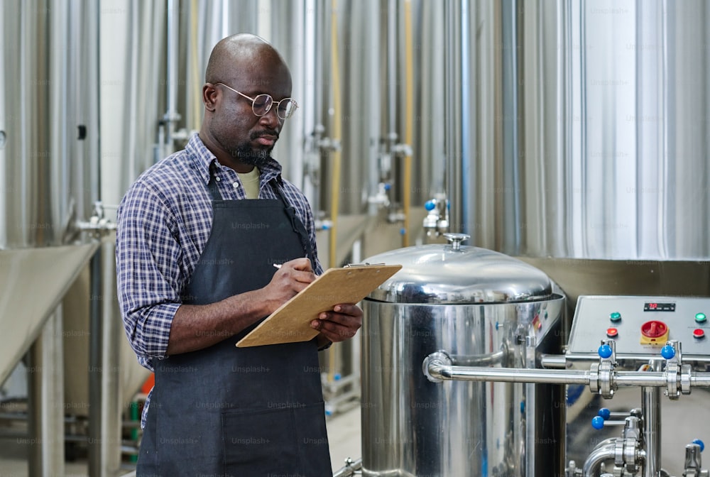 African American engineer examining new equipment and making notes in card during his work in factory