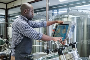 African American engineer controlling equipment with computer monitor during his work at brewery