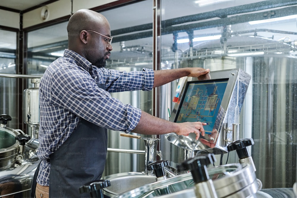 Ingeniero afroamericano controlando equipos con monitor de computadora durante su trabajo en la cervecería