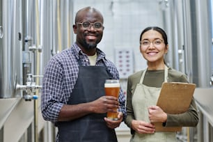 Portrait d’un couple de brasseurs souriant à la caméra tout en dégustant une bière ensemble dans une brasserie
