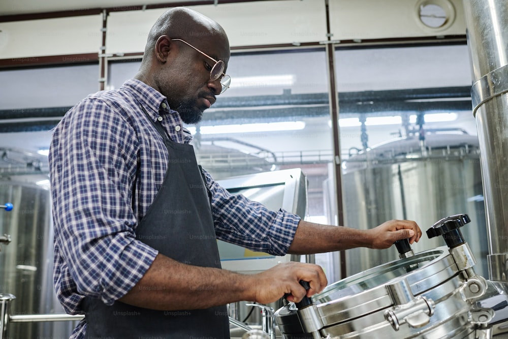 African American engineer concentrating on his work, he controlling equipment at brewey