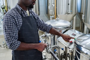 앞치마��를 입은 아프리카계 미국인 노동자가 양조 맥주 장비를 켜기 위해 버튼을 누르는 클로즈업