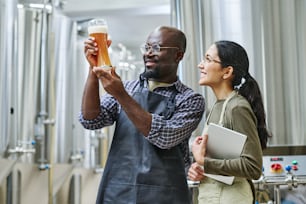 Afrikanischer Ingenieur untersucht frisches Bier im Glas und diskutiert mit seinem Kollegen über die Qualität
