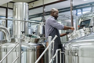 Uomo afroamericano che utilizza attrezzature speciali per produrre birra in laboratorio