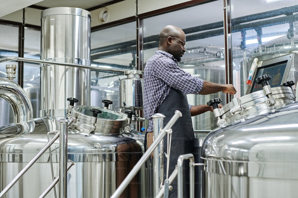 Hombre afroamericano usando equipo especial para elaborar cerveza en taller