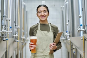 Retrato de un joven cervecero sonriendo a la cámara mientras degusta cerveza fresca en la cervecería