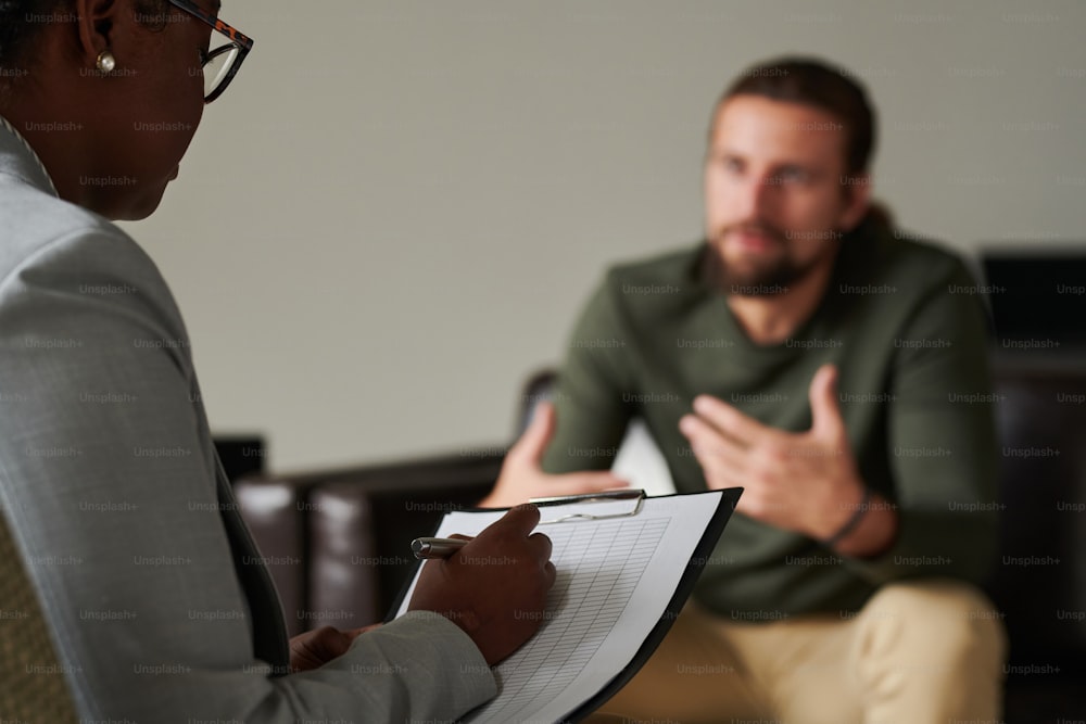 Close-up of African American psychotherapist making notes in card during psychotherapy with man