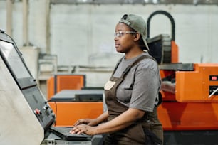 Afrikanische Bedienerin in Arbeitskleidung, die sich auf ihre Arbeit konzentriert, die Maschine in der Fabrik zu steuern