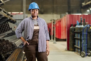 Portrait of African professional heavy industry worker in helmet standing in workshop of factory