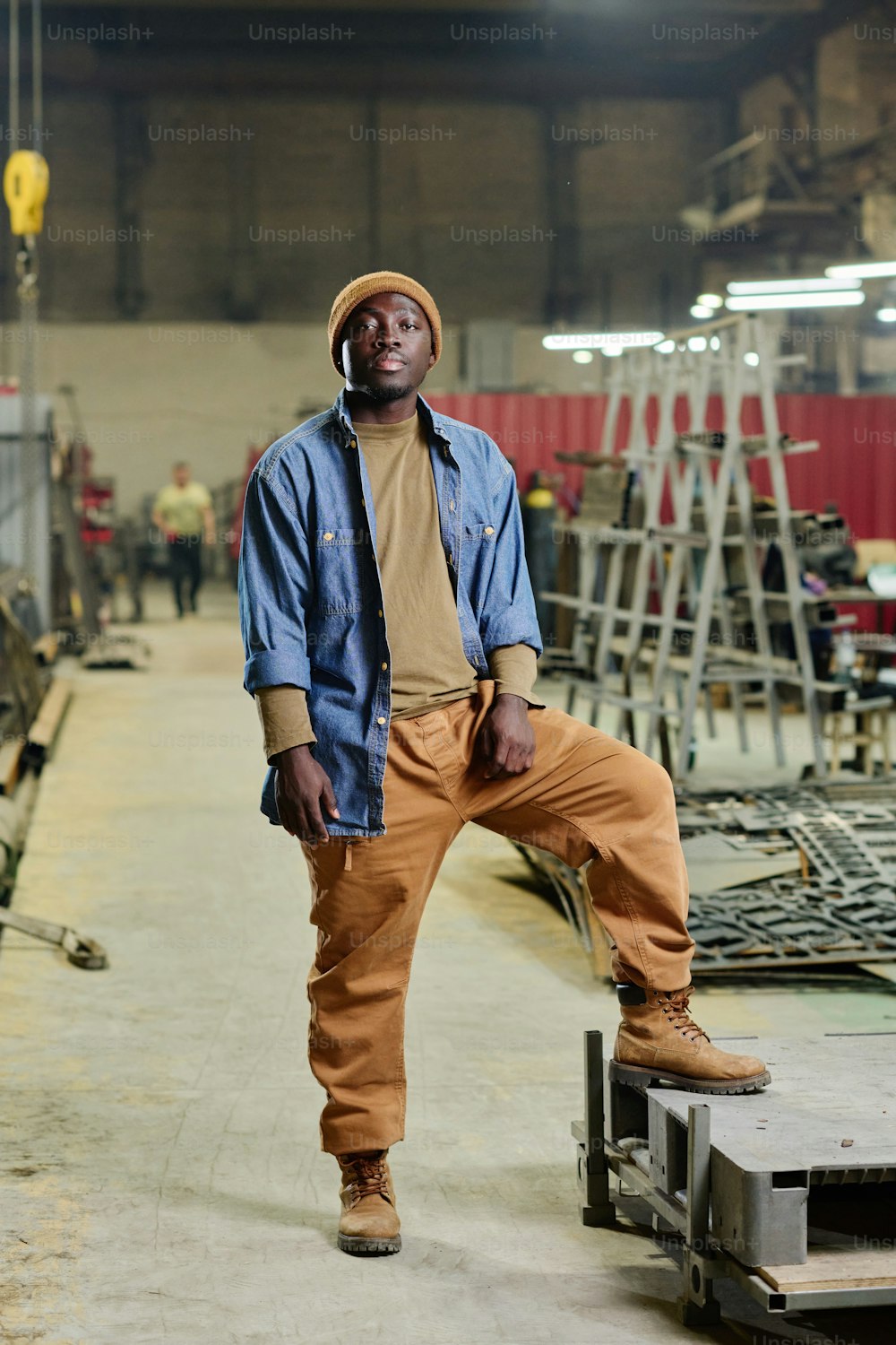 Portrait of African young man in workwear looking at camera standing in workshop of factory