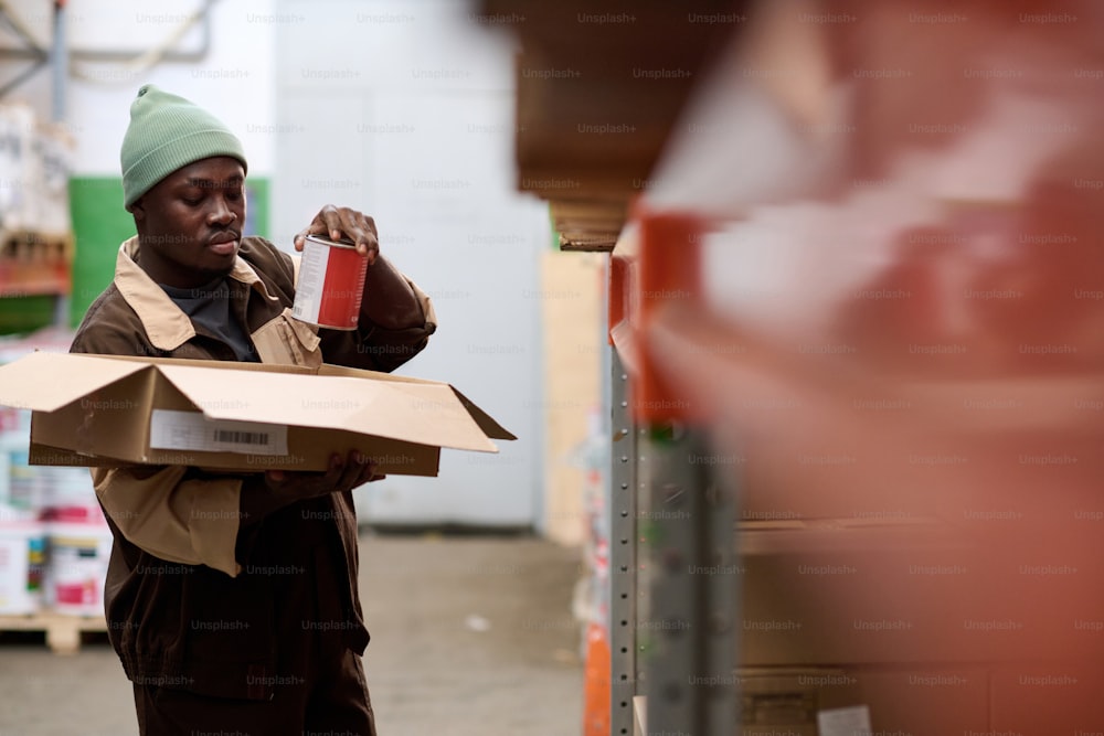 African American warehouse worker taking goods from shelves and packing them in box before shipping