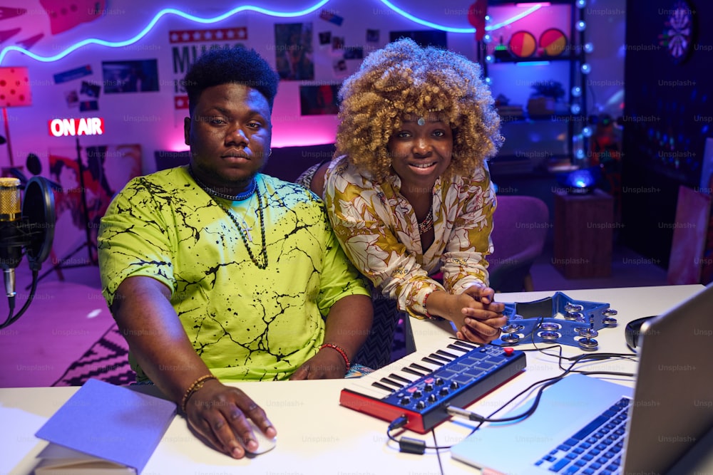 Young Gen Z African American man and woman wearing fashionable casual clothes working together on music album in home recording studio looking at camera
