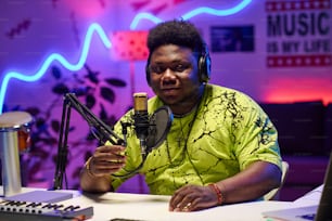 Young African American man wearing headphones adjusting microphone to start podcast or broadcast recording in home studio