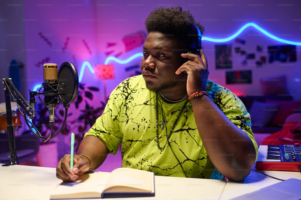 Porträt eines stilvollen jungen afroamerikanischen Musikers, der am Schreibtisch sitzt, Musiktitel hört und an Texten arbeitet