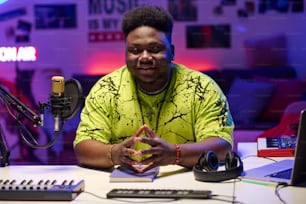 Stilvoller junger schwarzer Mann in neongelbem T-Shirt, der am Schreibtisch im Amateur-Sendestudio sitzt