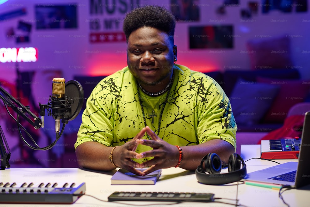 Stylish young Black man wearing neon yellow T-shirt sitting in at desk in amateur broadcasting studio