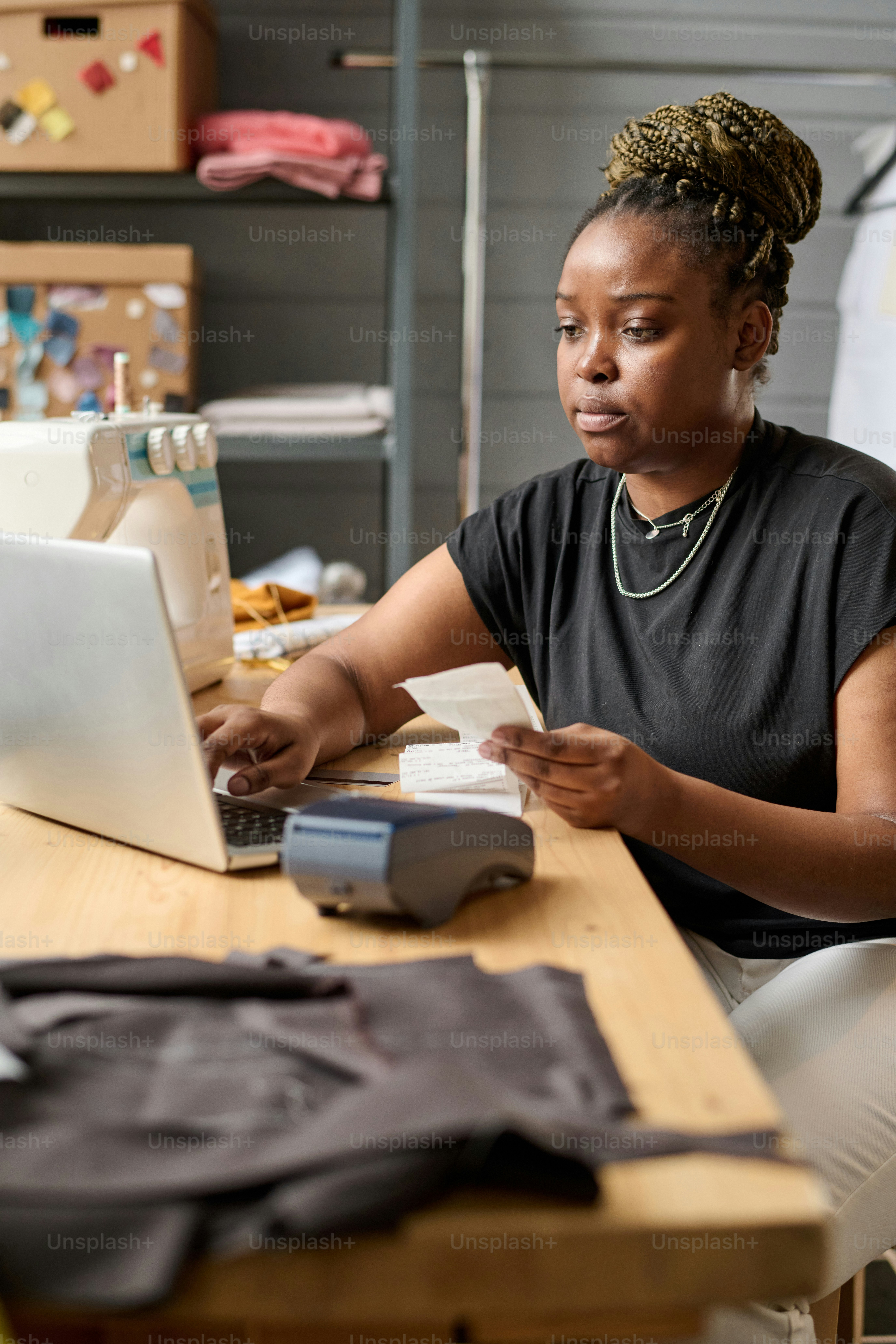 Young serious female warehouse worker checking receits of payment for online orders while sitting by workplace in front of laptop