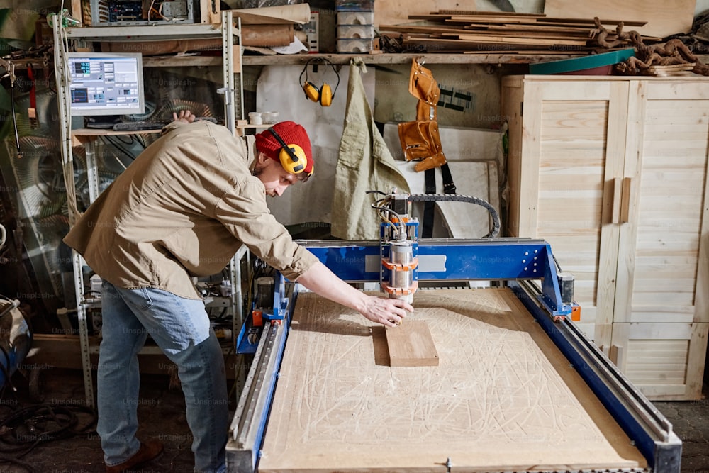 Carpinteiro profissional ajustando a fresadora CNC para fazer detalhes de madeira na oficina de marcenaria