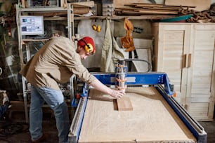 Professional carpenter adjusting CNC milling machine to make wooden details in woodworking workshop