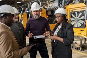 Équipe commerciale discutant du partenariat dans l’industrie de la construction debout dans un entrepôt avec des machines en arrière-plan