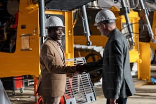 Multiracial engineers in work helmets shaking hands and making a deal during a meeting at an equipment manufacturing plant