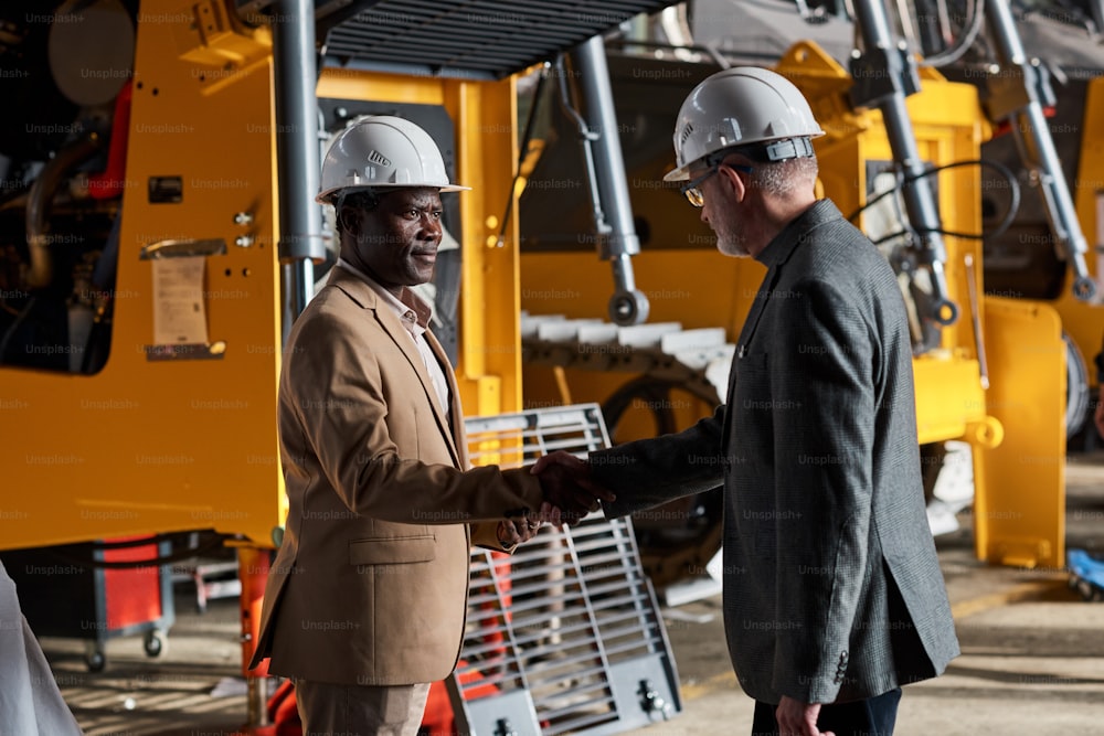 Multiracial engineers in work helmets shaking hands and making a deal during a meeting at an equipment manufacturing plant