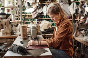 Junge Schneiderin sitzt an ihrem Arbeitsplatz mit einer Nähmaschine, um in der Fabrik Kleidung aus Leder herzustellen